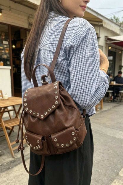 Brown faux-leather backpack worn over one shoulder, showing the curved flap and two front pockets.