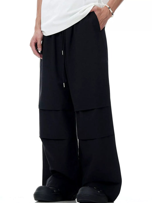 Black men's wide-leg drawstring trousers, front view showing layered leg panels; pictured top and shoes are not included.