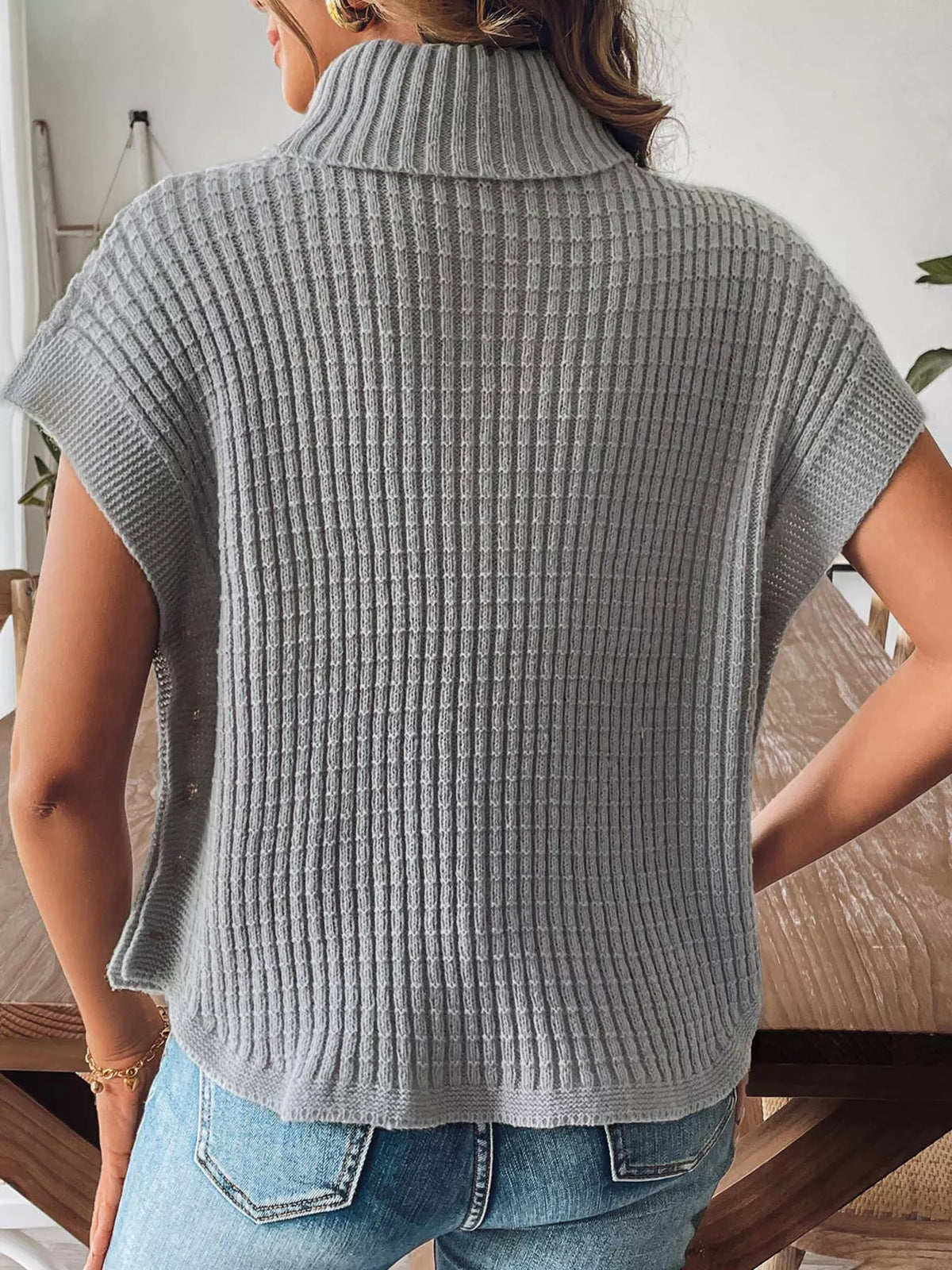 Back view of the grey ribbed turtleneck sweater vest; jeans are styling only.