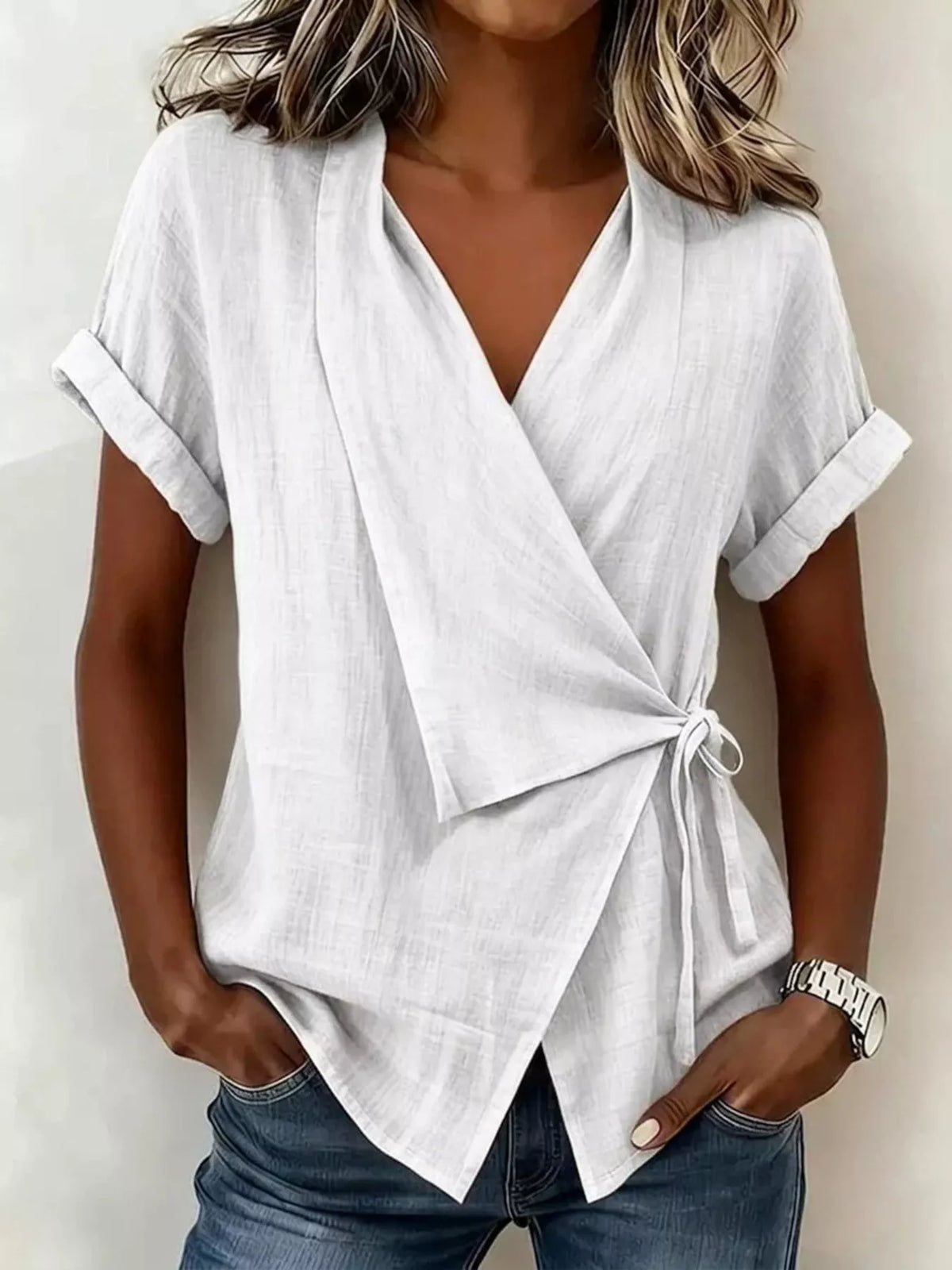 White wrap top on a model, front view with a V-neck, cuffed short sleeves, side tie and overlapping hem.