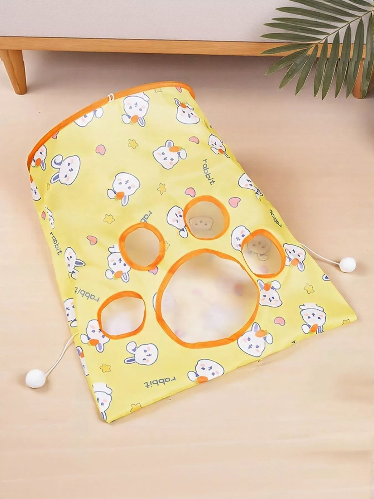 Rabbit Pattern yellow tunnel folded flat, showing orange-trimmed play openings and pom-poms