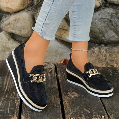 Side view of black slip-on wedge loafers with chain-style trim.