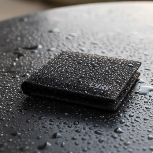 Closed black COR Surf bifold wallet resting on a wet surface with water droplets.