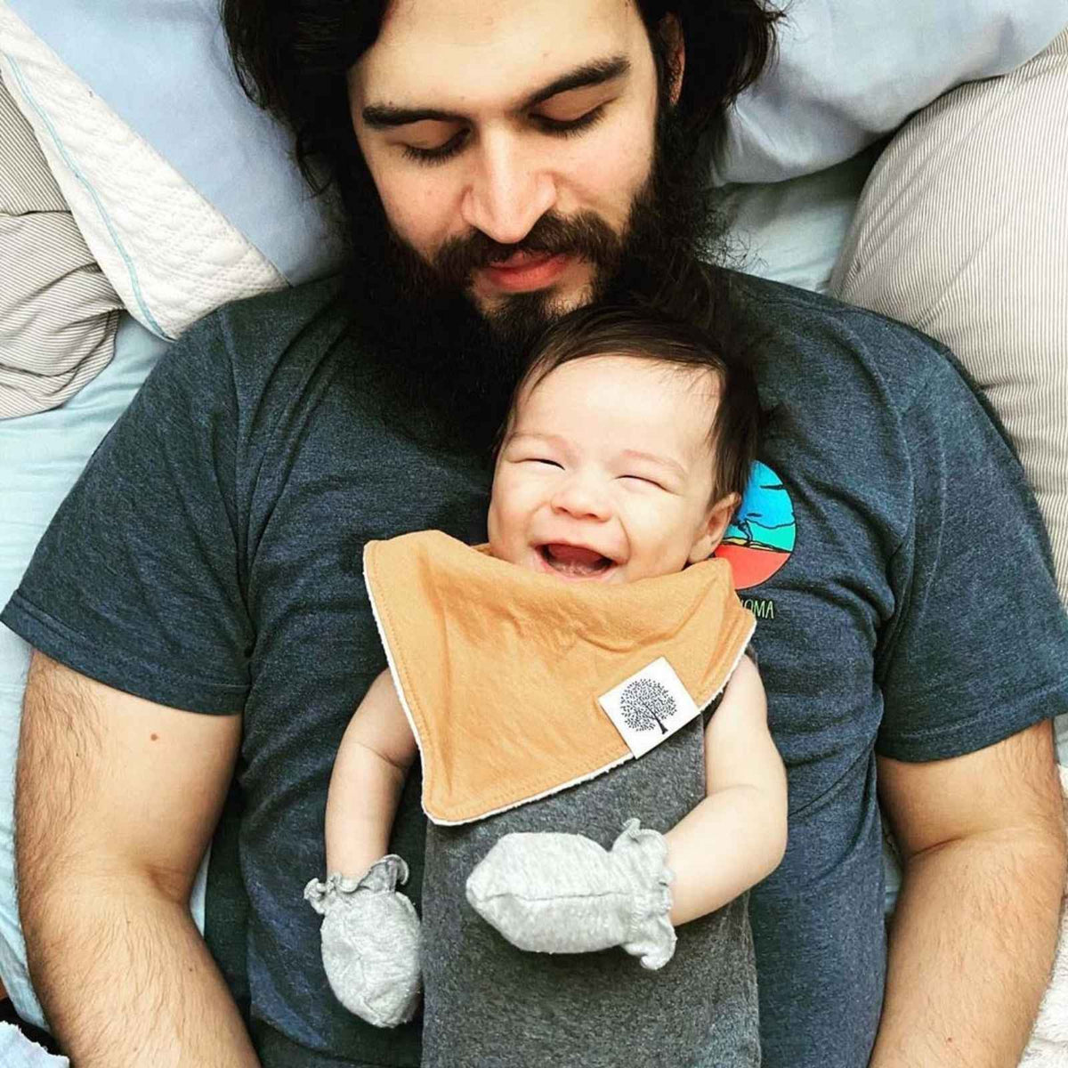 Baby wearing the tan bib from the Estes eight-bib set while held by an adult.