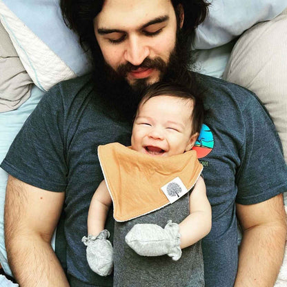 Baby wearing the tan bib from the Estes eight-bib set while held by an adult.