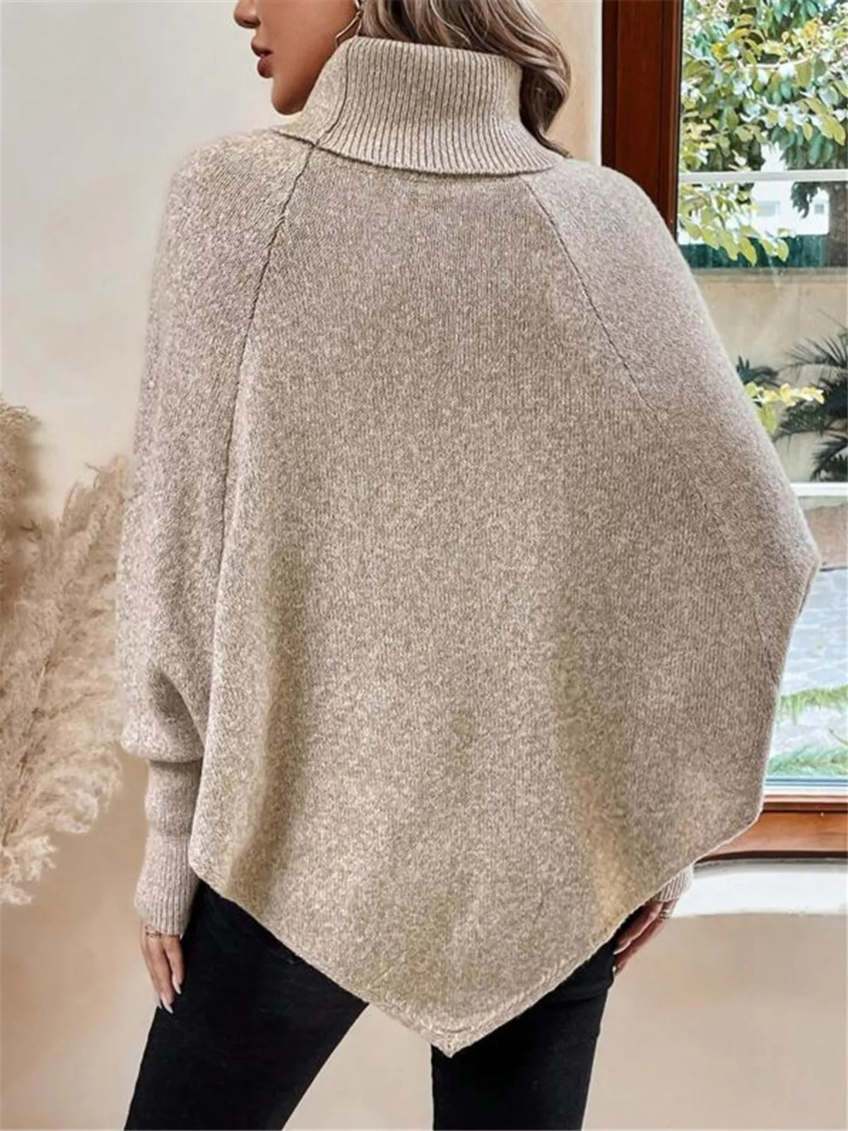 Warm beige/oatmeal cable-knit turtleneck cape sweater. Rear/side view showing cape back and shoulder buttons. Styling accessories are not included.