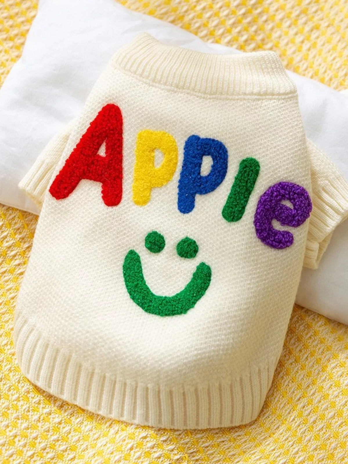White pet sweater with colorful Apple lettering and a smile graphic, shown flat.