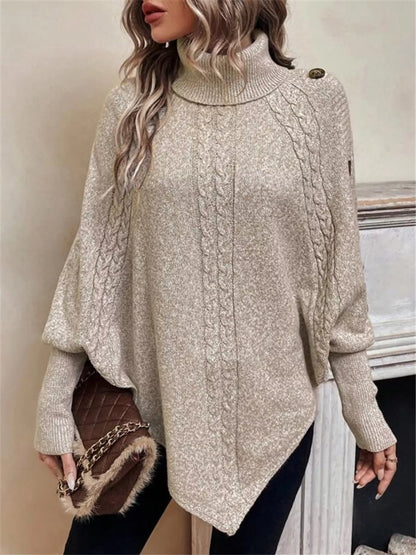 Warm beige/oatmeal cable-knit turtleneck cape sweater. Front three-quarter view, model in black pants. Styling accessories are not included.