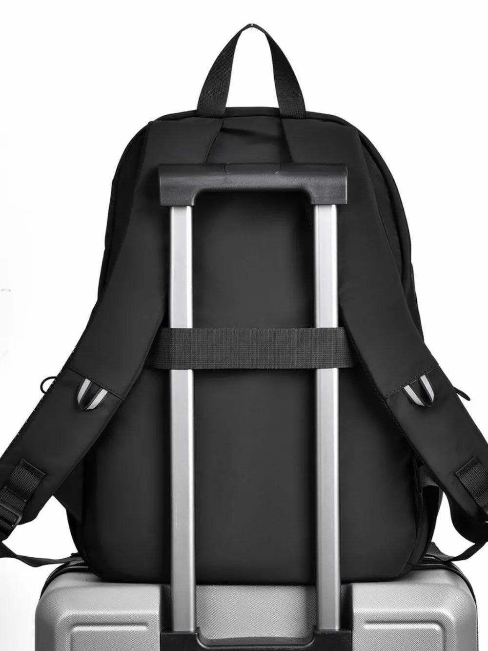 Back of the black backpack with its trolley strap over a rolling suitcase handle; suitcase not included