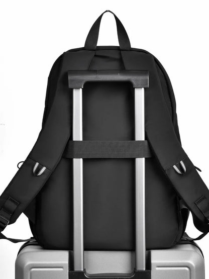 Back of the black backpack with its trolley strap over a rolling suitcase handle; suitcase not included