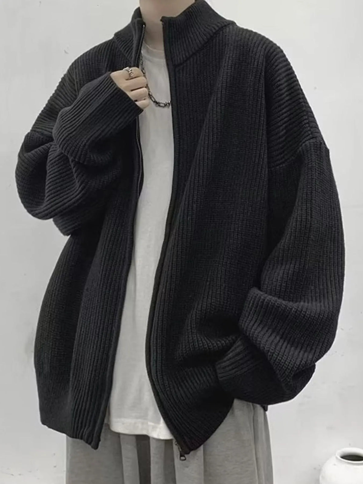 Front of the black ribbed cardigan worn open, showing its stand collar, long sleeves and zipper.