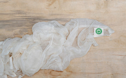 Natural cotton cheesecloth spread on a wooden surface, showing its hanging tag.