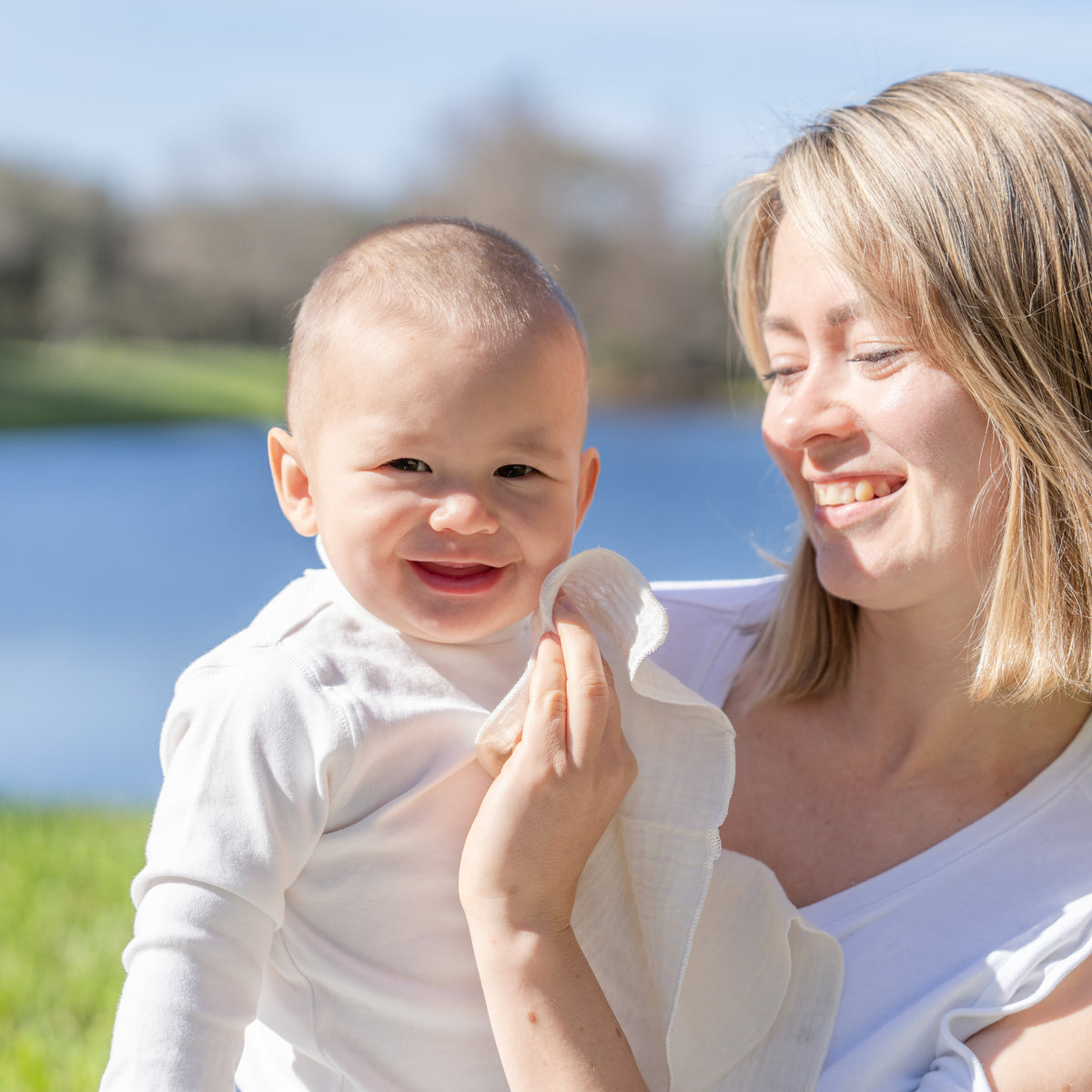 Parent holding a baby outdoors while using a cotton wipe on the baby's face