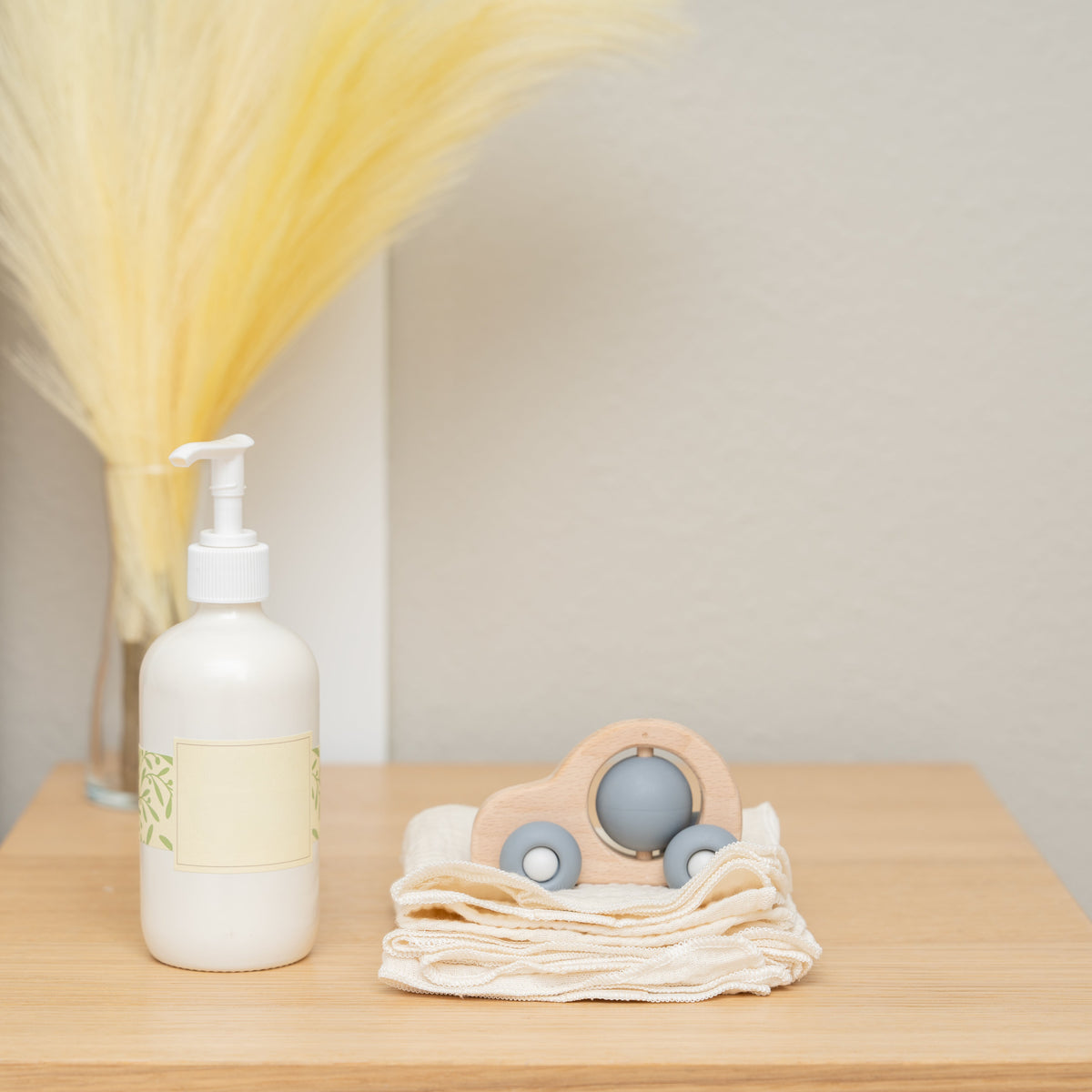 Cream cotton wipes on a wooden table; bottle, toy and stems are styling props