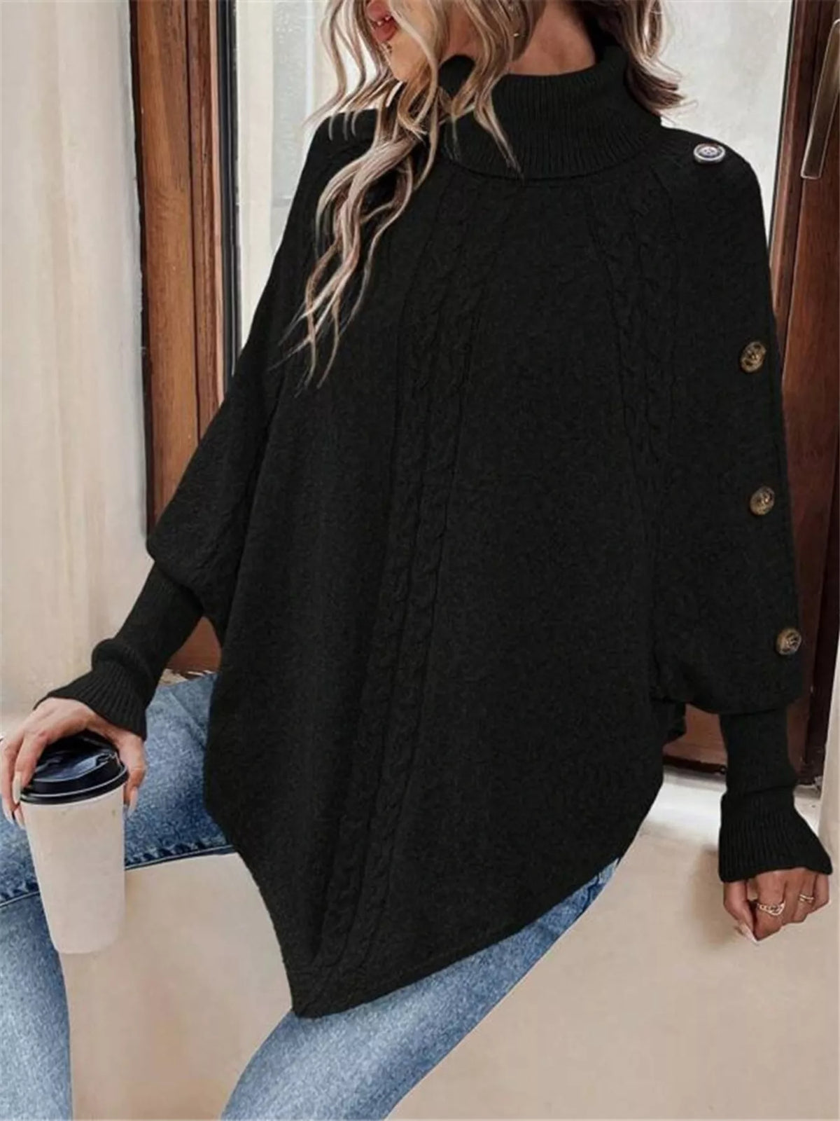 Black cable-knit turtleneck cape sweater. Front three-quarter view, model in blue jeans. Styling accessories are not included.
