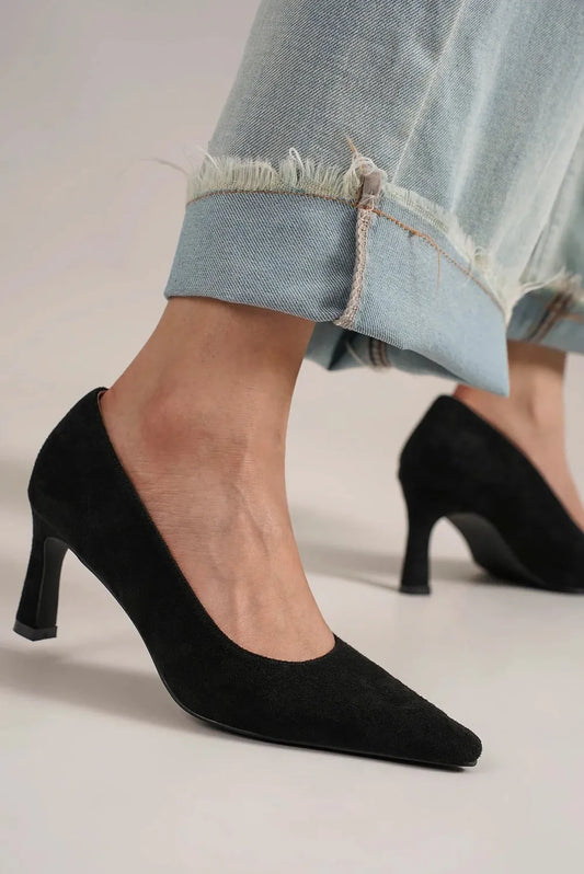 Black faux-suede pointed-toe pumps shown on feet beneath cuffed jeans; shoes only.