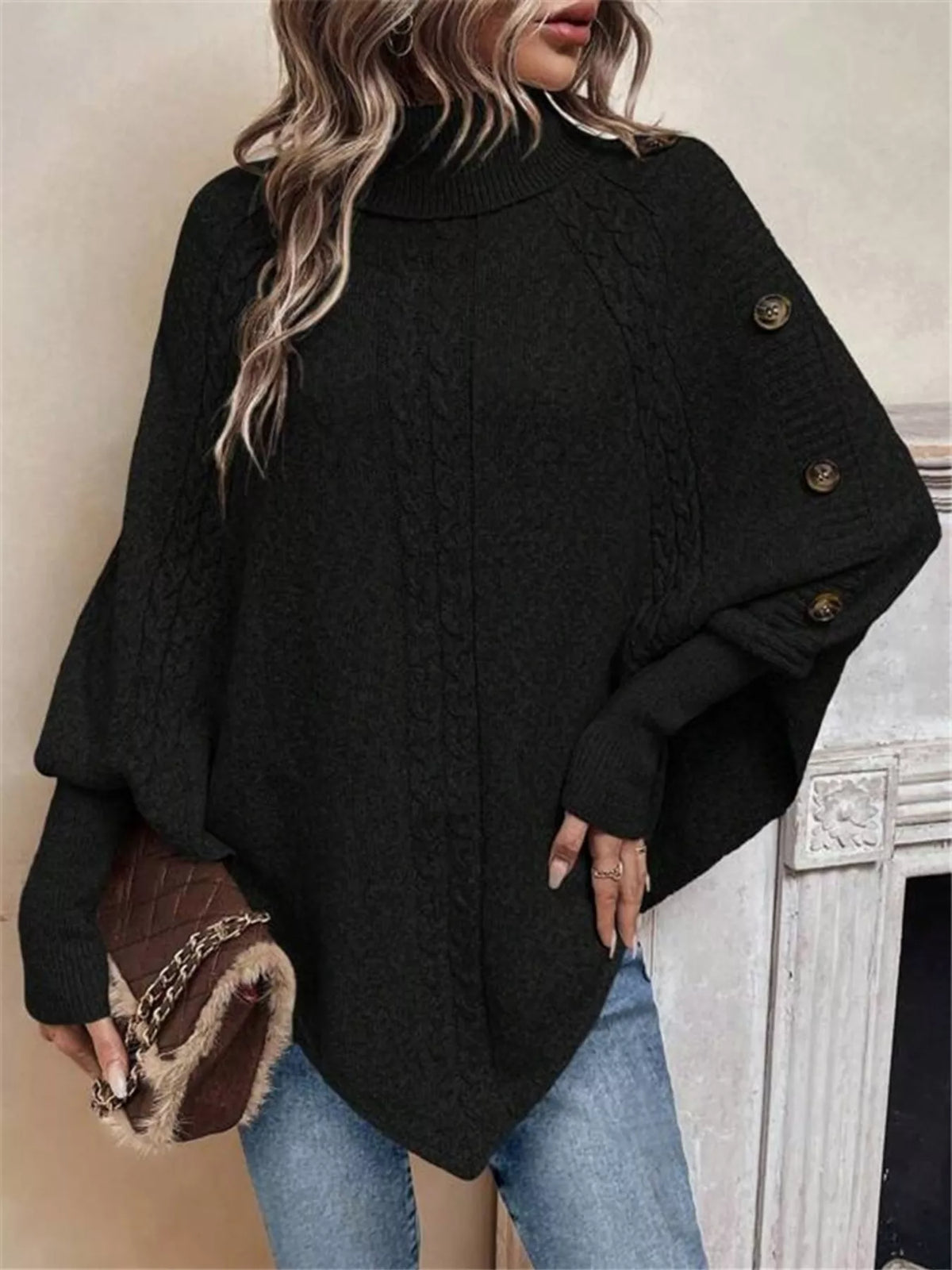 Black cable-knit turtleneck cape sweater. Front view, model in blue jeans. Styling accessories are not included.