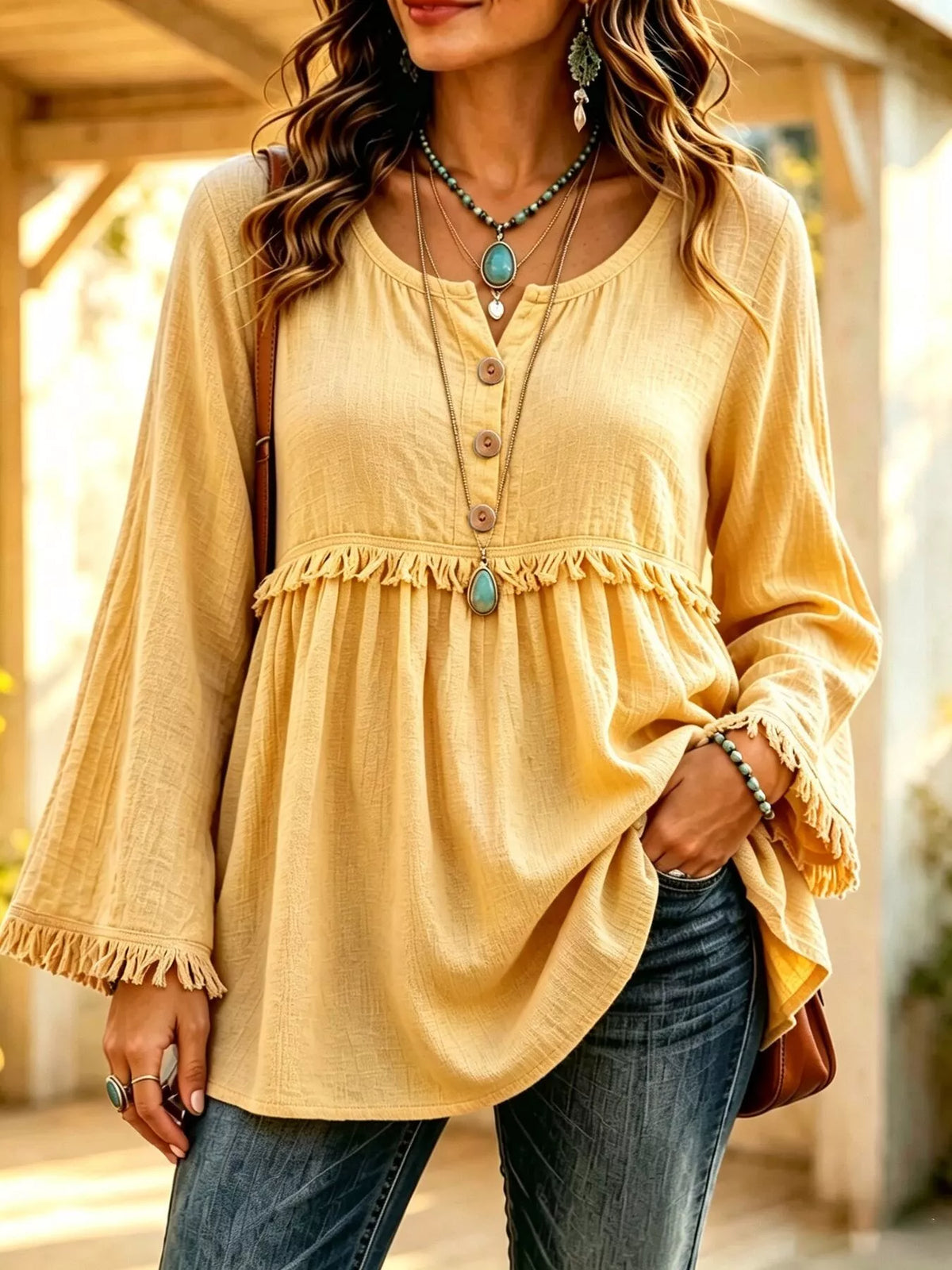 Yellow blouse on a model, front view with three-button neckline, gathered body and fringe-trimmed sleeves.