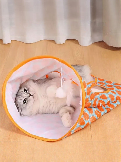 Cat lying inside an orange circle-print tunnel, viewed through the opening.