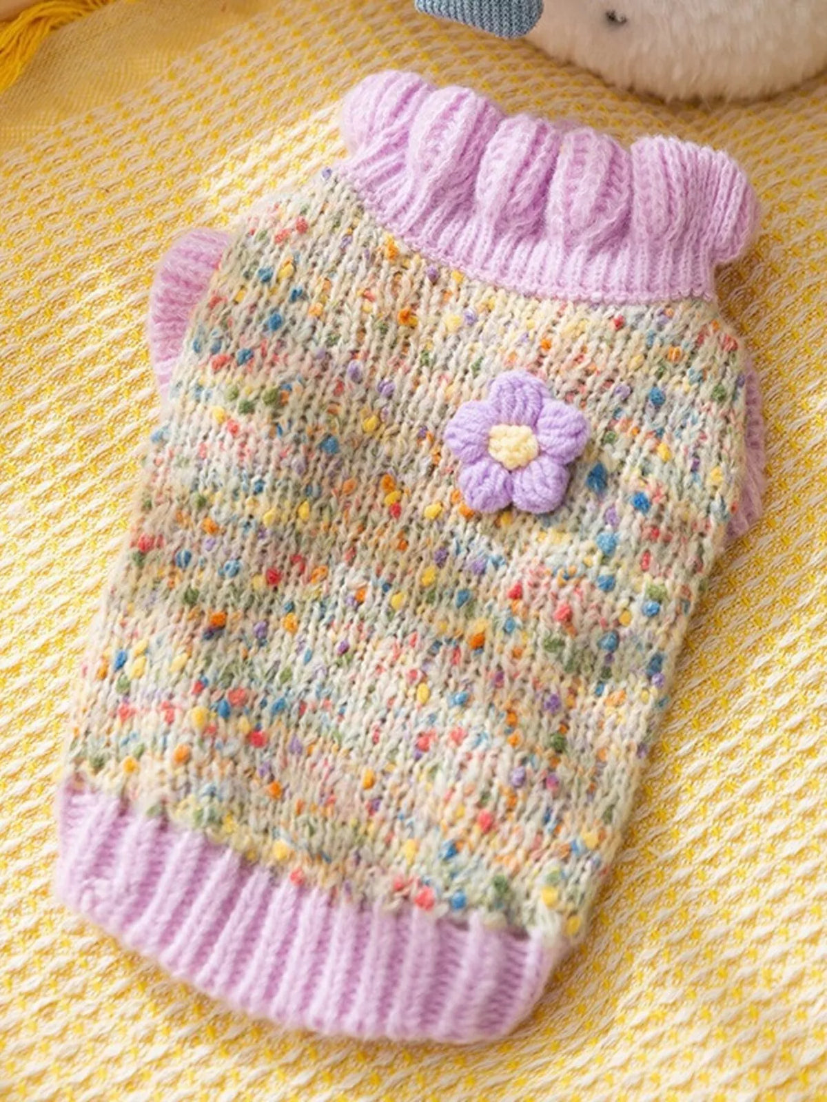 Pastel-speckled pet sweater with lilac collar, cuffs and flower applique, shown flat.
