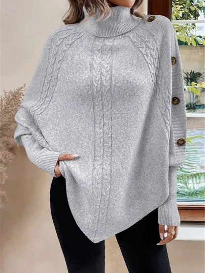 Light gray cable-knit turtleneck cape sweater. Front view with arm extended, model in black pants. Styling accessories are not included.