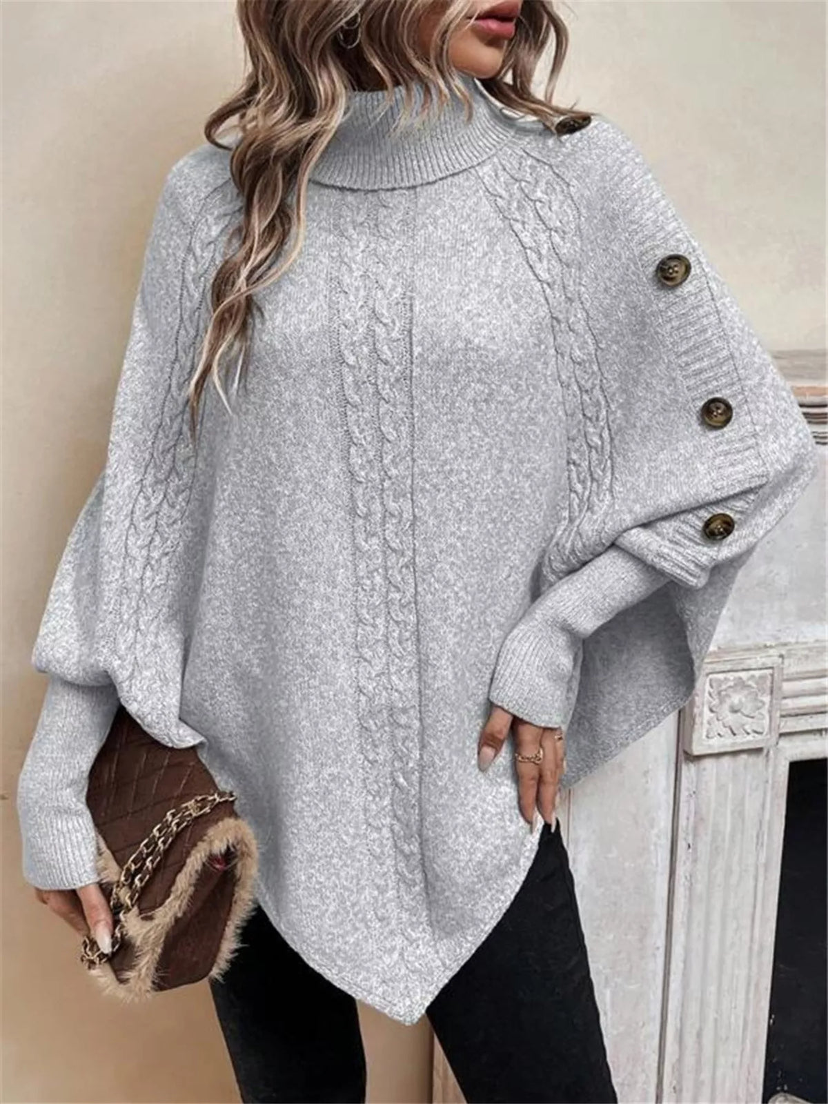 Light gray cable-knit turtleneck cape sweater. Front/side view, model in black pants. Styling accessories are not included.