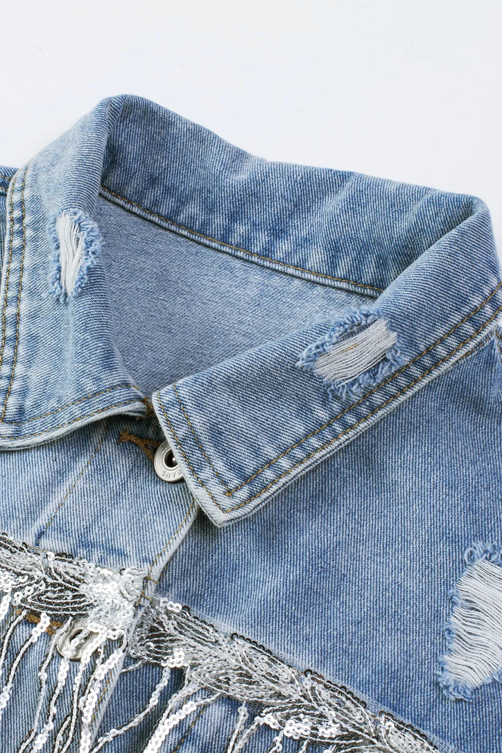 Angled close-up of the denim jacket collar, stitching, distressed patches and top button.