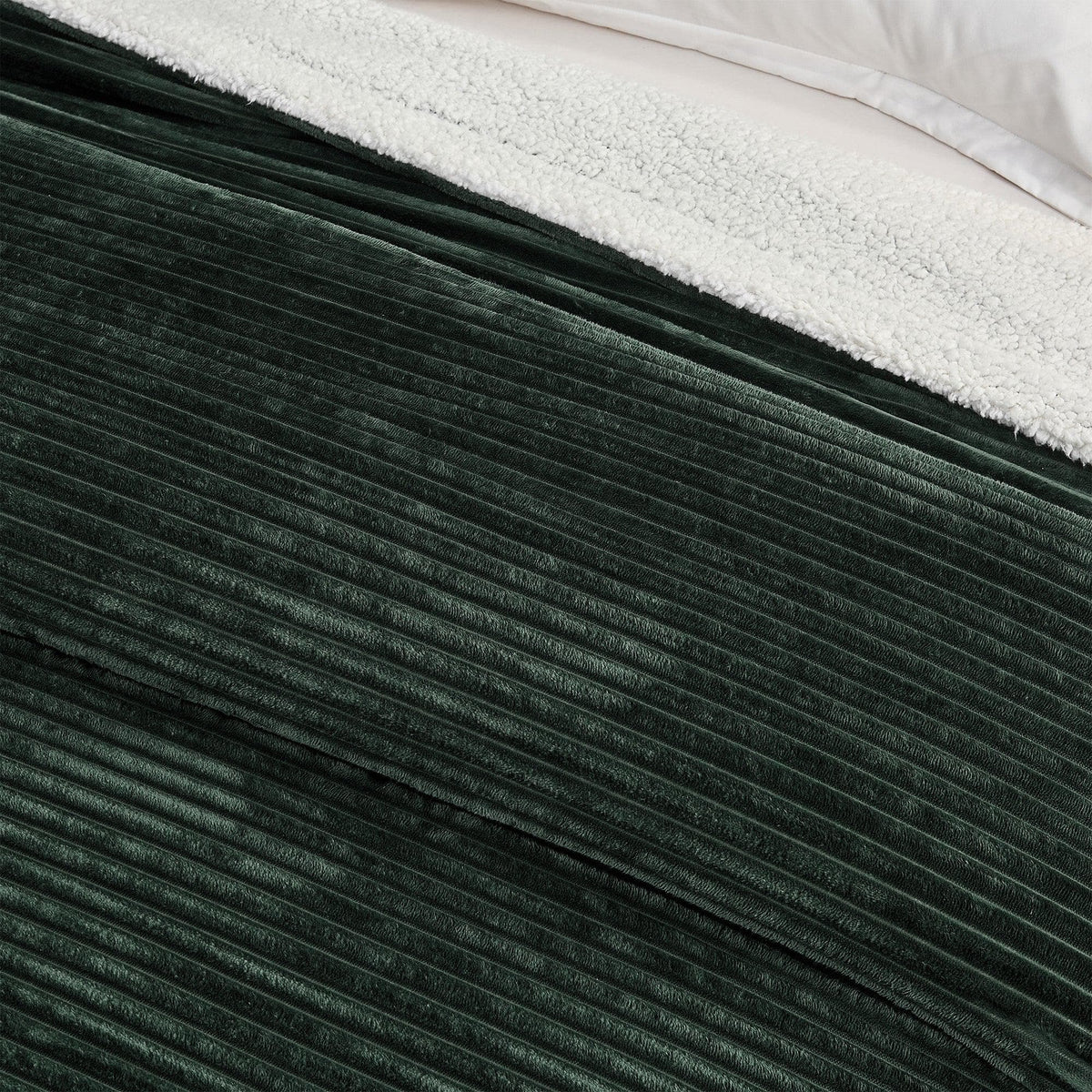 Close-up of the forest green ribbed face and pale sherpa reverse of the blanket.
