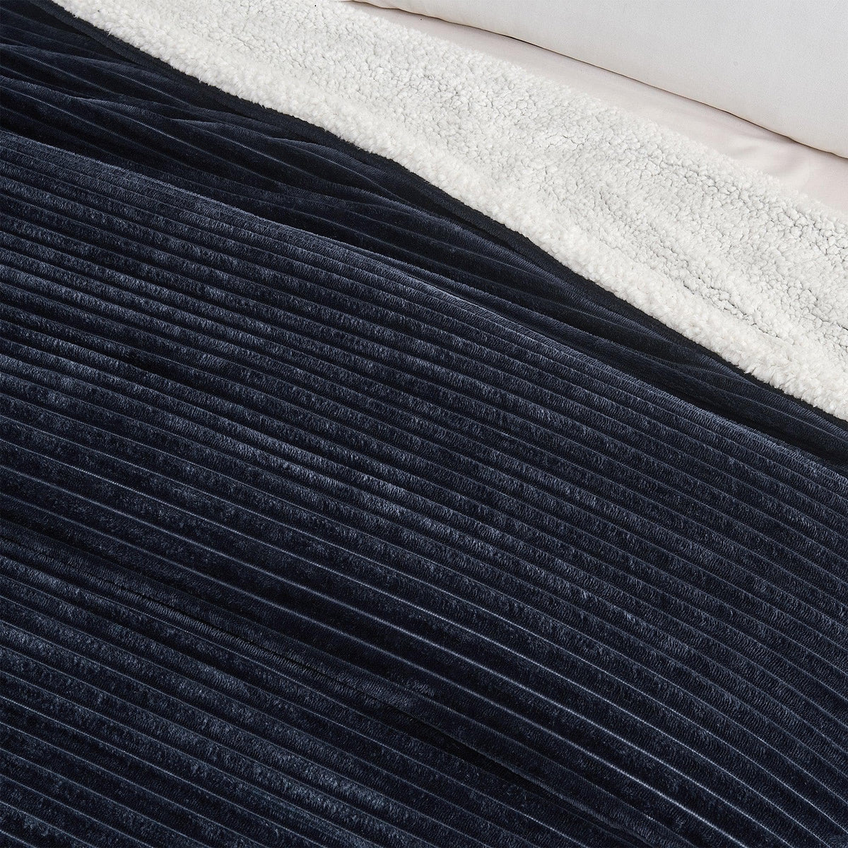 Close-up of the navy ribbed face and pale sherpa reverse of the blanket.