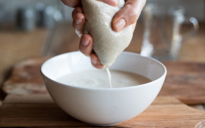 Nut milk being strained through a cotton bag; bowl not included
