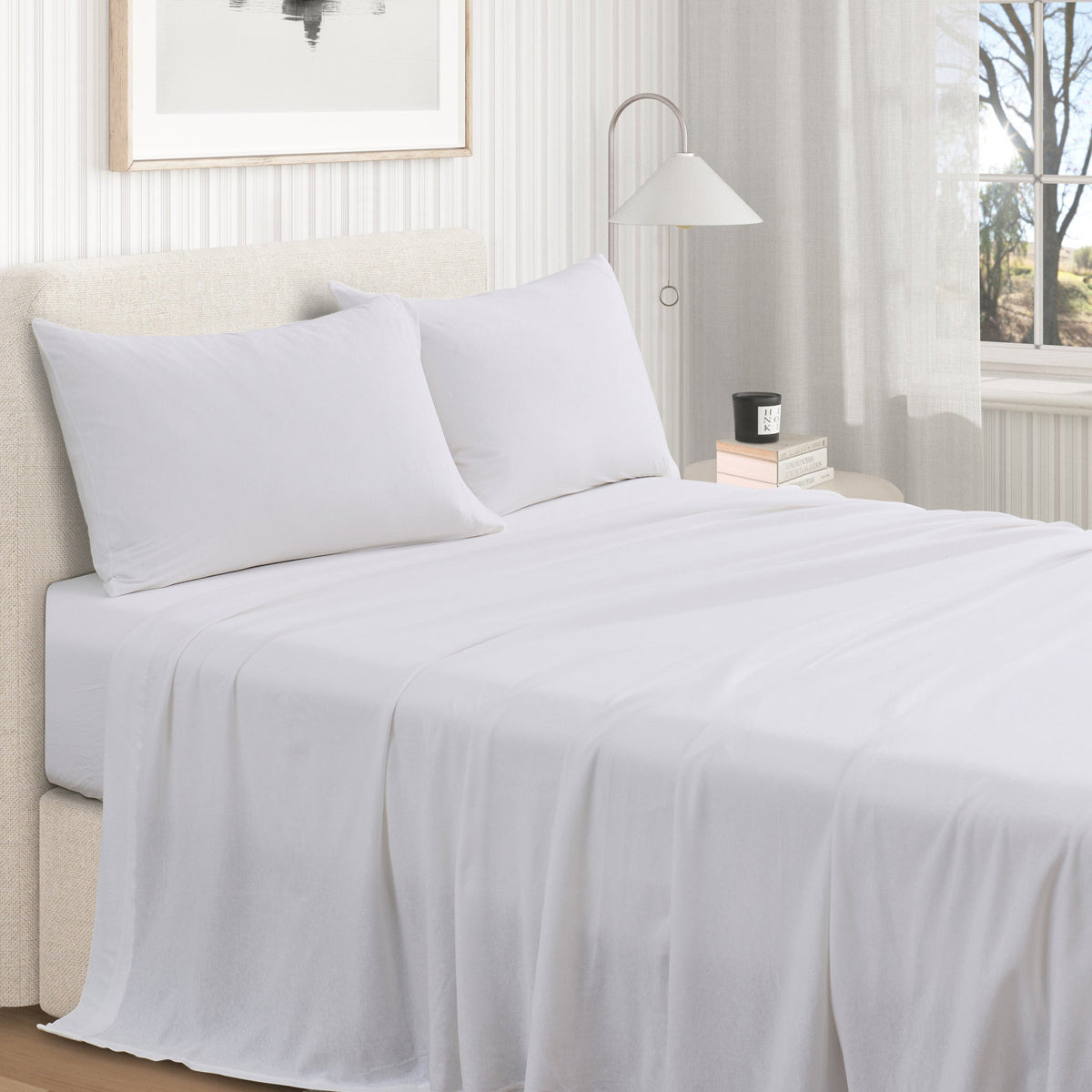 White cotton jersey knit sheet set shown on a made bed from a second room angle, with matching pillows and draped sheet.