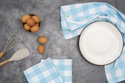 Aqua-and-white plaid kitchen towels beside baking ingredients and utensils; food and utensils not included.