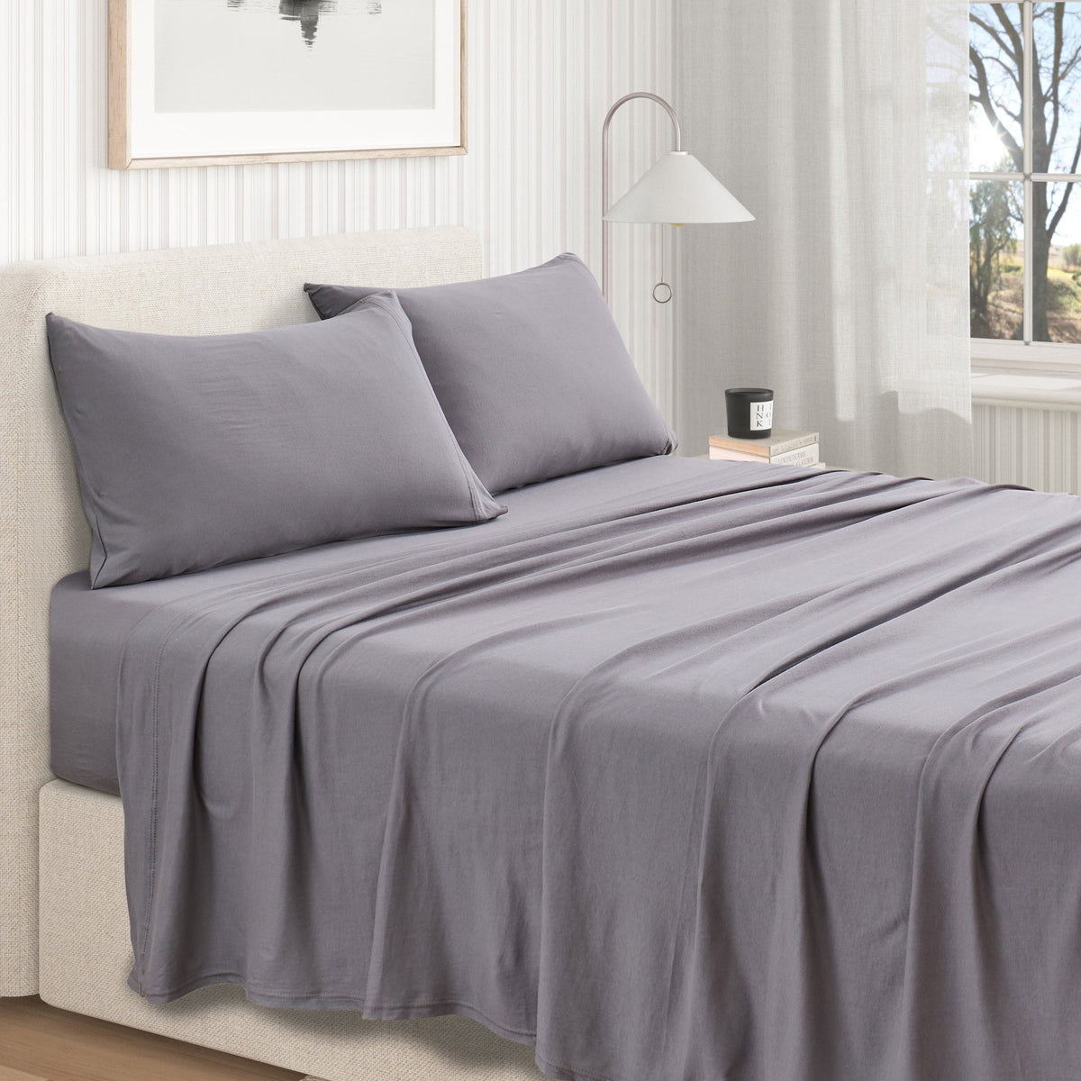 Charcoal cotton jersey knit sheet set shown on a made bed from a second room angle, with matching pillows and draped sheet.