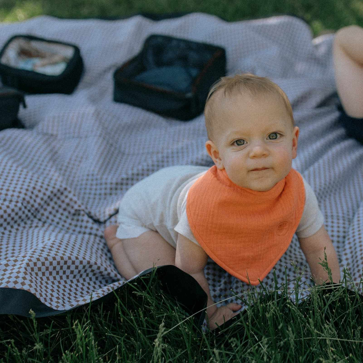 Orange Estes muslin bandana bib worn by a baby; clothing and blanket not included.
