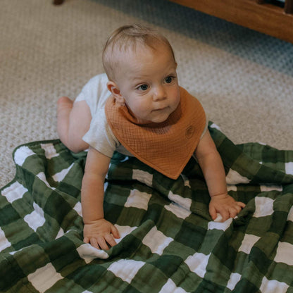 Tan Estes muslin bandana bib worn by a baby; clothing and blanket not included.