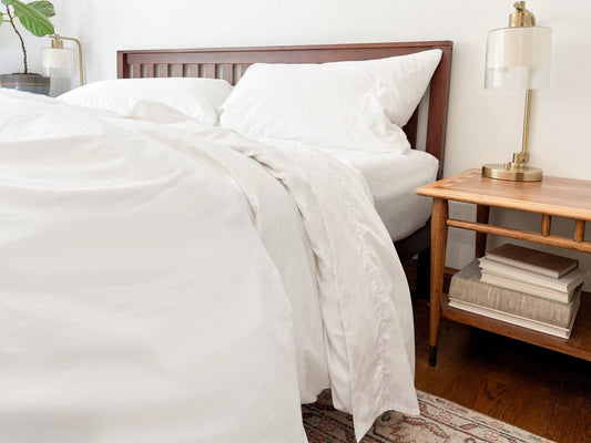 White percale bedding arranged on a bed with a wooden headboard and bedside table