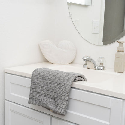 Gray cotton muslin towel draped over a bathroom sink; bathroom accessories are not included.
