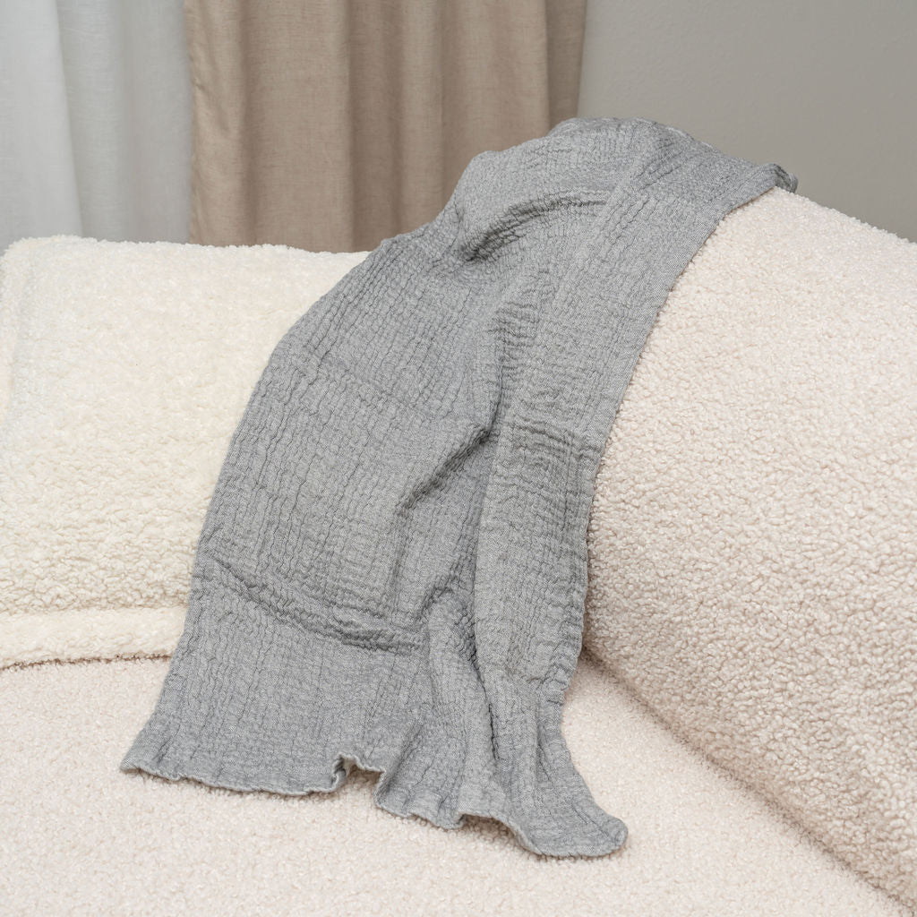 Gray cotton muslin towel draped over a cream sofa; sofa is not included.