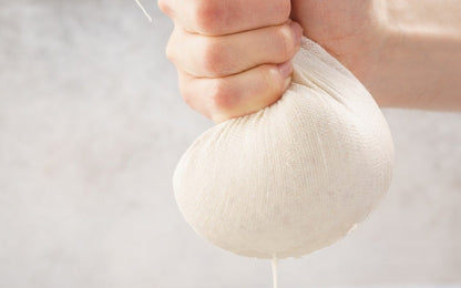 Hand holding cotton cheesecloth wrapped around food during straining; food is not included.