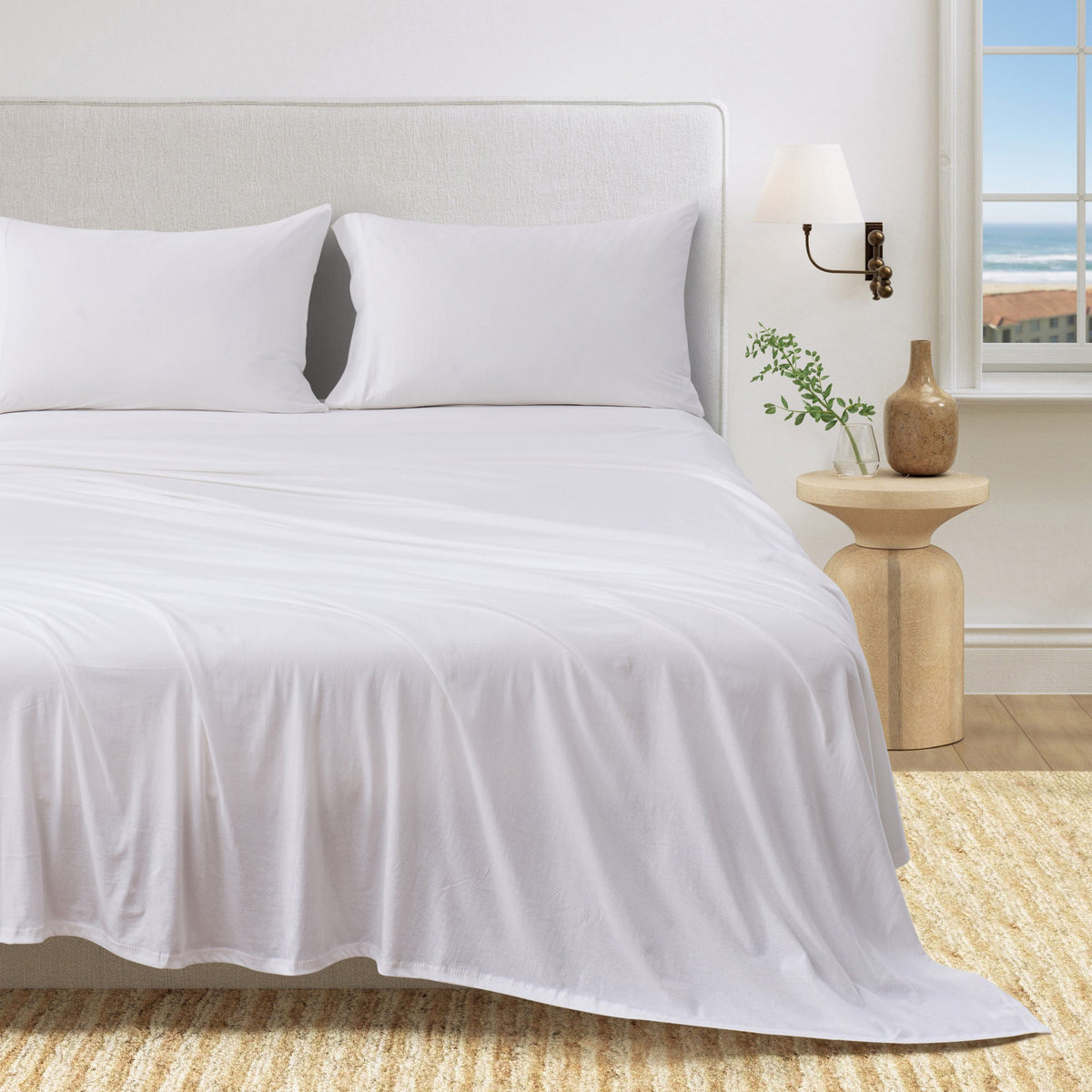White cotton jersey knit sheet set shown on a bed with matching pillowcases in a bright bedroom.