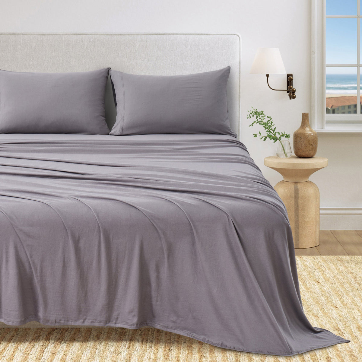 Charcoal cotton jersey knit sheet set shown on a bed with matching pillowcases in a bright bedroom.